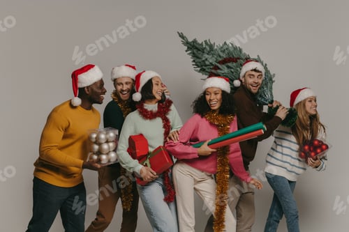 Preview: Happy young people carrying Christmas tree and various ornaments while walking on studio
