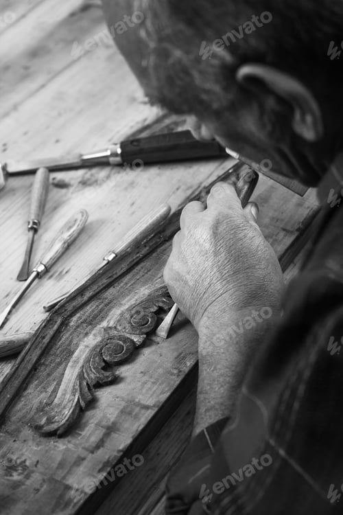 Preview: Senior carpenter working with a hammer, chisel and wood carving tools.