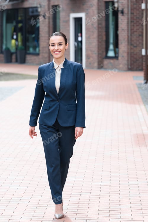 Preview: beautiful businesswoman walking on street and looking away