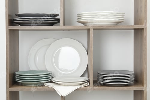 Preview: Shelving unit with different plates near white wall indoors