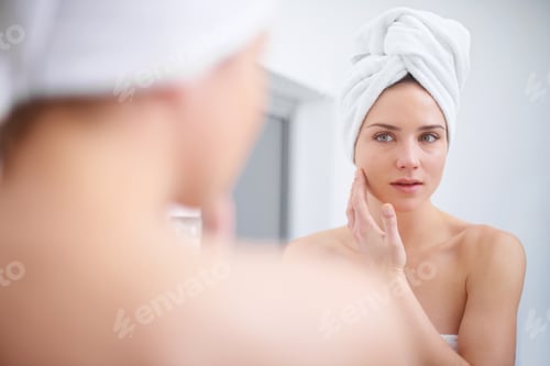 Preview: Personal beauty regime. A woman looking in her bathroom mirror with a towel on her head.