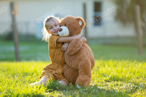 Preview: Pretty child girl tenderly embracing her teddy bear friend outdoors on green grass lawn