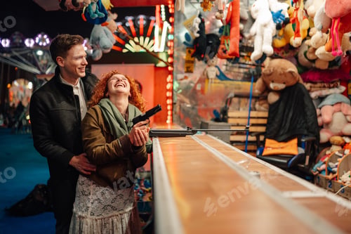 Preview: Happy couple enjoying shooting game at fairground