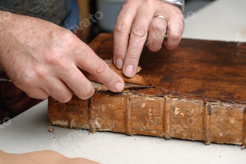 Preview: Close up of hands of senior male traditional bookbinder removing leather from book