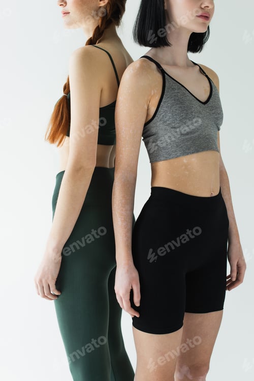 Preview: Cropped view of sportswomen with vitiligo and freckles standing back to back isolated on grey