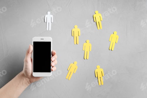 Preview: Woman holding smartphone over grey table with paper people, top view. Loneliness concept
