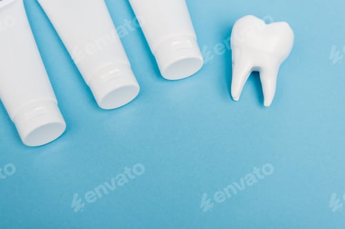 Preview: Top view of tooth model and tubes with toothpaste on blue background