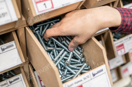 Preview: persons hand choose suitable bolt or screw from the crate in hardware store b