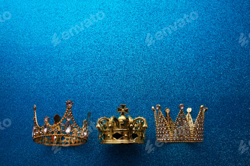 Preview: Epiphany Day or Dia de Reyes Magos concept. Three gold crowns on blue sparkling background