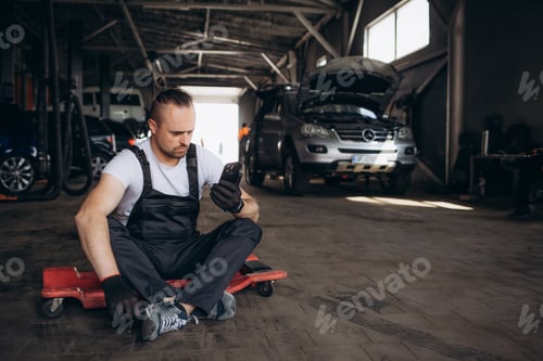 Preview: Young professional technician car mechanic man 20s in blue overalls white t-shirt use hold mobile