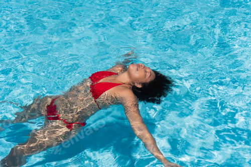 Preview: Young woman floating and relaxing in a clear blue swimming pool