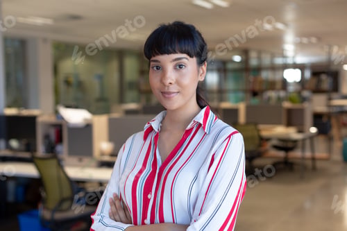 Preview: Portrait of confident young biracial businesswoman with arms crossed at modern workplace