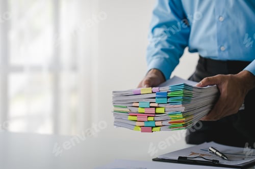 Preview: Businessman working on stacks of documents to search for information and check documents on office d