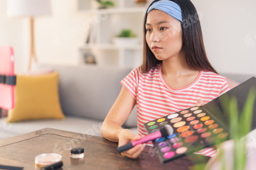 Preview: Young asian woman using a palette of eye shadows to apply makeup
