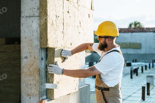 Preview: builder in protective helmet and googles doing insulation of wall at construction site