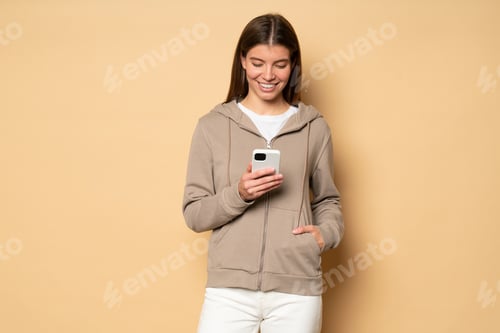 Preview: Woman in sport hoodie watching online fitness tutorial on her phone on brown background