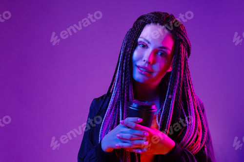 Preview: Portrait of a woman with long afro braids holding a cup of coffee against purple neon background