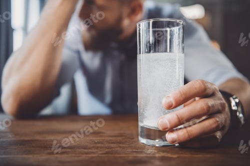 Preview: tired man with hangover with medicines after party at home