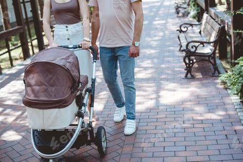 Preview: cropped image of parents walking with baby carriage in park