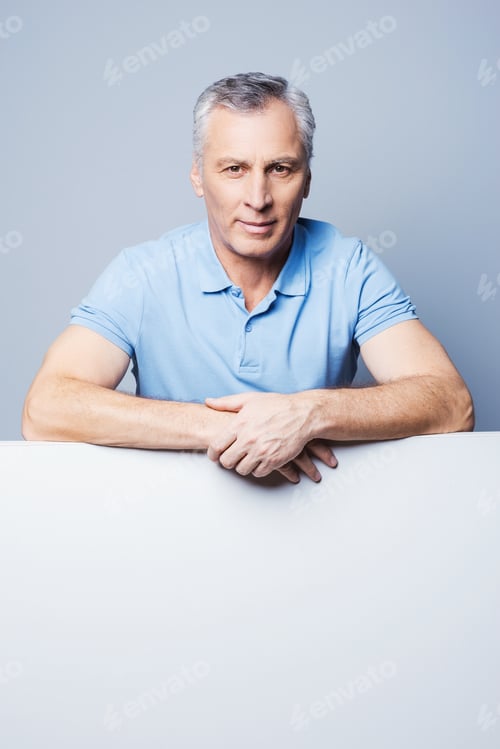 Preview: Under copy space. Handsome senior man leaning at copy space while standing against grey background