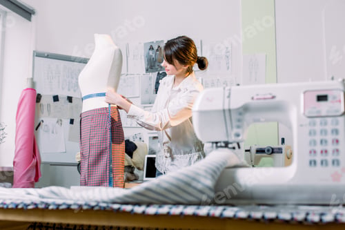 Preview: attractive brunette woman fashion designer seamstress measuring mannequin in her fashion atelier