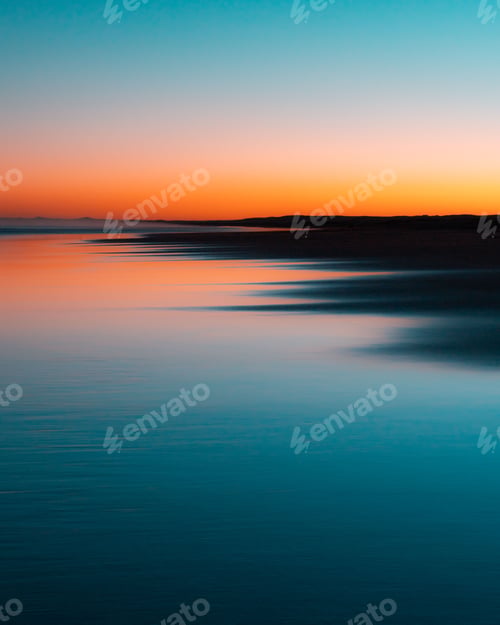 Preview: Vertical shot of a gradient sky during sunset perfectly reflecting on water with land silhouettes