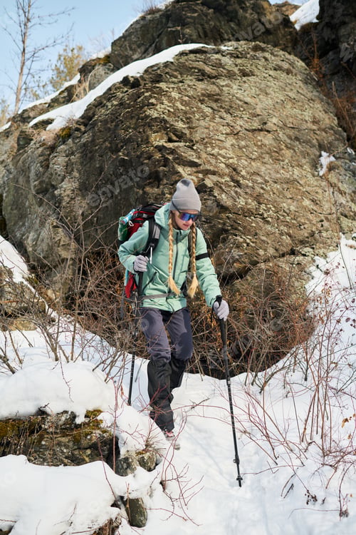 Preview: Young Adult Woman Hiking with Trekking Poles in Snowy Mountains