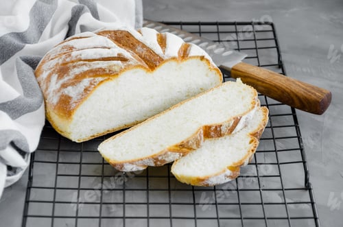 Preview: Homemade round bread with knife on a dark concrete background. Horizontal orientation.
