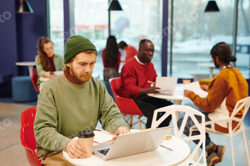 Preview: Serious bearded businesswoman with glass of coffee looking at laptop display