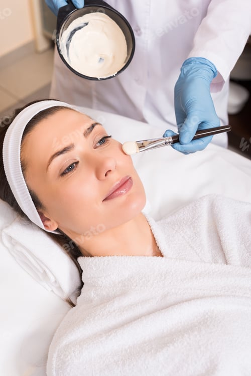 Preview: beautician applying cosmetic mask on woman cheek with cosmetic brush at beauty salon