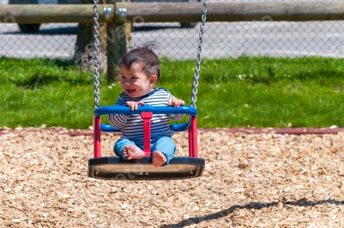 Preview: Selective focus shot of a happy Swiss-Thai baby boy swinging in a sunny park outside