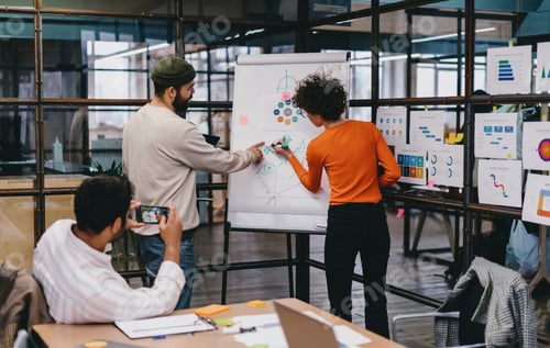 Preview: Focused colleagues drawing on board and taking photograph in office