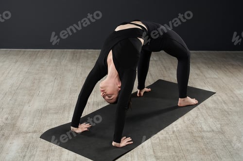 Preview: Flexible slim woman doing backbend in yoga studio.