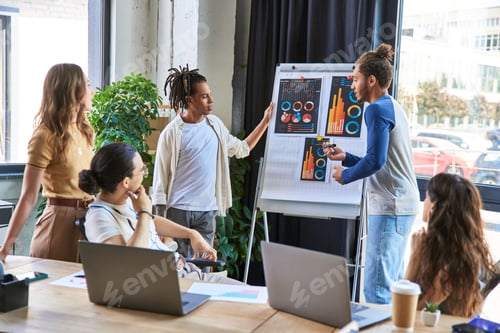 Preview: multicultural colleagues discussing startup project near flip chart with infographics in office
