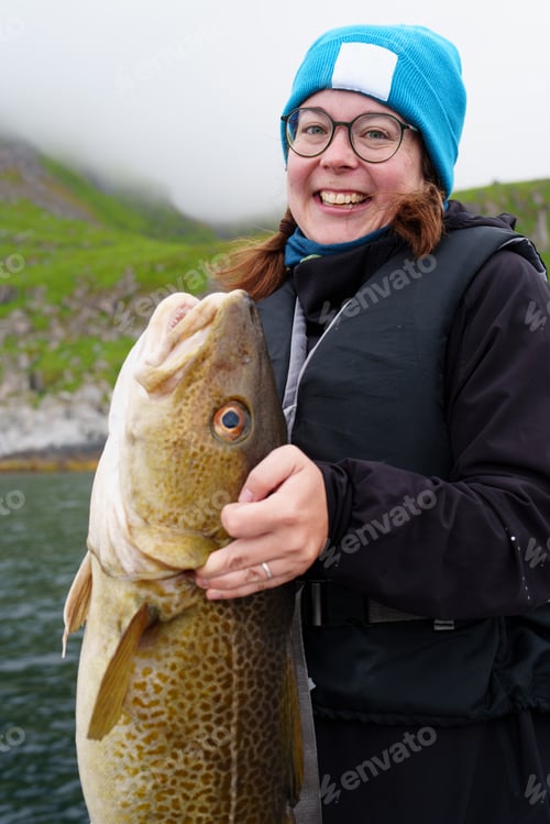 Preview: Happy young woman holding big arctic cod. Norway happy fishing. Fisherwoman with cod fish in hands