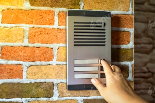 Preview: Close up of woman using intercom at building entrance.