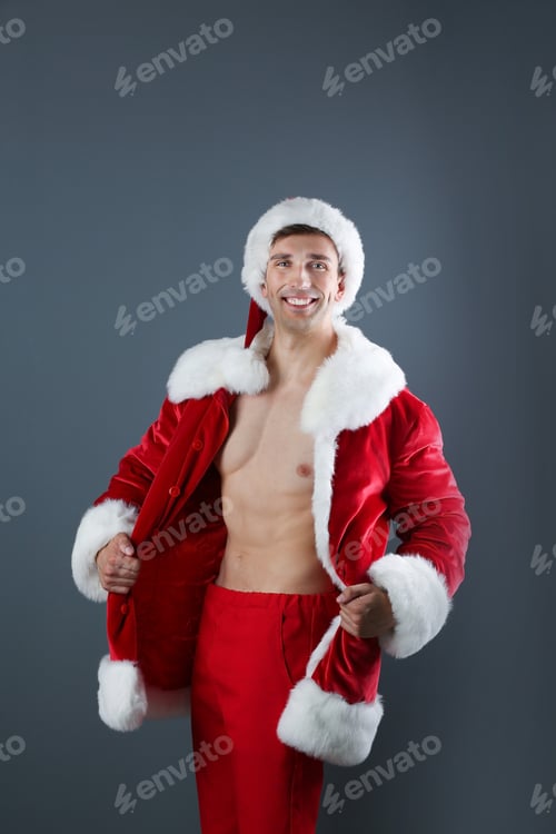 Preview: Young muscular man in Santa Claus costume on gray background