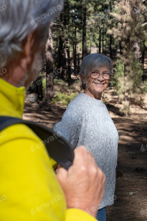 Preview: Attractive senior woman looking at her husband walking in the forest holding his hands