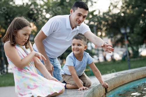 Preview: Dad with his son and daughter near the fountain in the summer park.