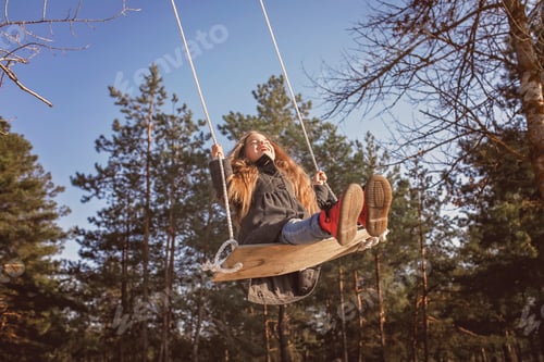 Preview: Smiling girl with tresses hair in grey coat flying on a swing against blue sky