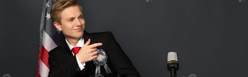 Preview: smiling emotional man pointing with finger on tribune with american flag on black background