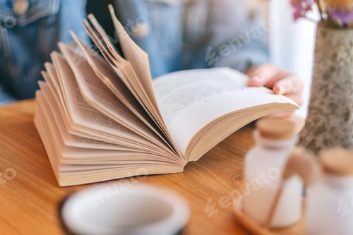 Preview: Closeup image of a woman holding and reading a vintage novel book with coffee cup on wooden table
