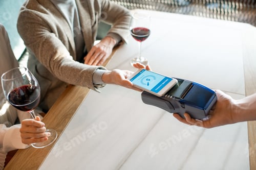 Preview: Young man holding smartphone over payment terminal while paying for dinner