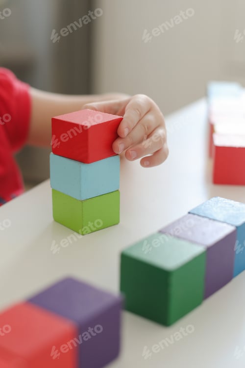 Preview: Child playing and building with colorful wooden bricks on white table, flatlay