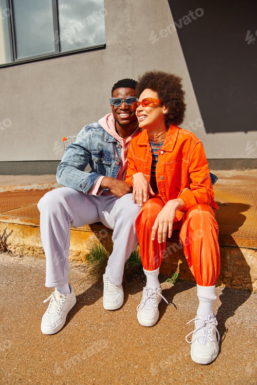 Preview: Smiling young african american man in sunglasses hugging trendy best friend in bright outfit