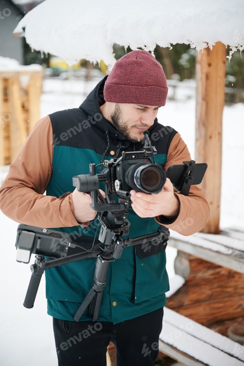 Preview: videographer man with camera mounted on gimbal stabilizer equipment in winter.