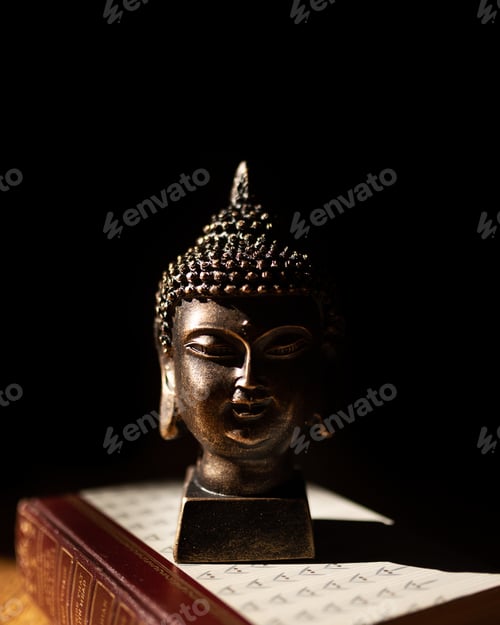 Preview: Vertical shot of a Buddha head statue placed on a book