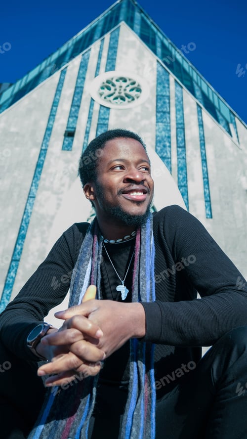 Preview: Young African man in a black outfit walking in a street posing in front of a glass paneled building