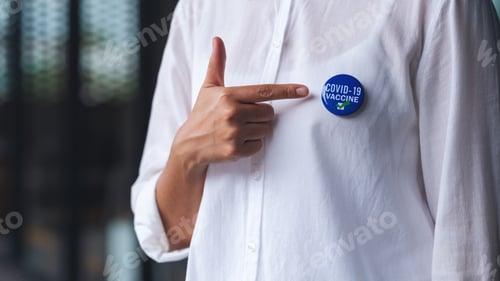 Preview: Closeup image of a woman showing and pointing finger at Covid-19 vaccinated sign brooch on shirt