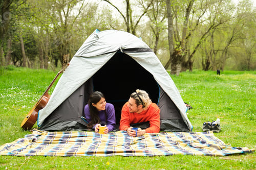 Preview: A couple is laying in a tent in a grassy field, camping